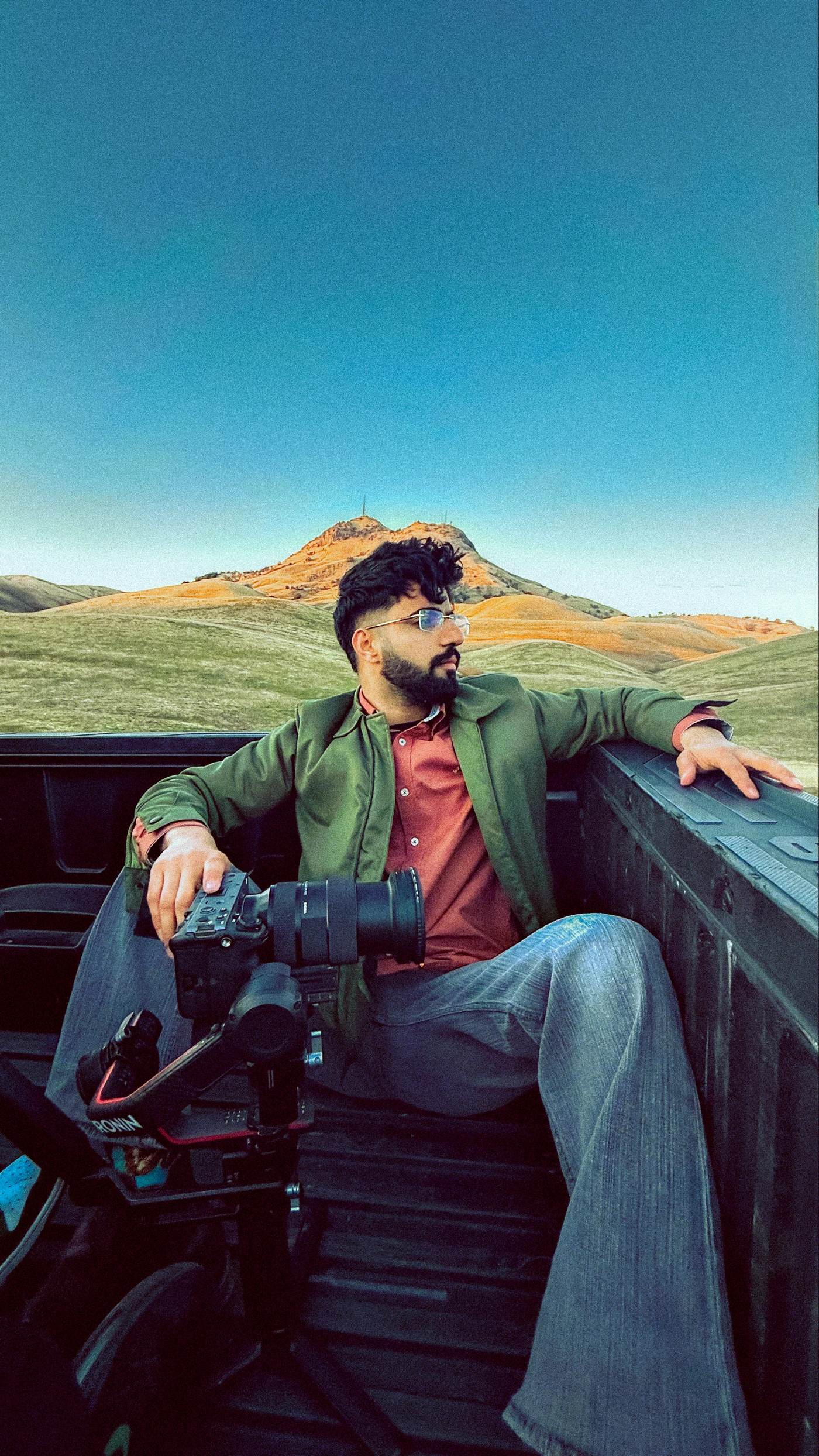 Manraj Brar with his camera, seated in a truck surrounded by rolling hills